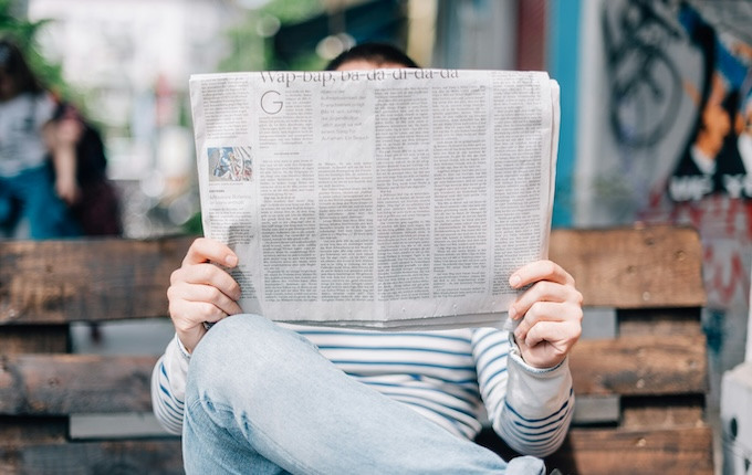 Man reading a newspaper while sitting on bench.