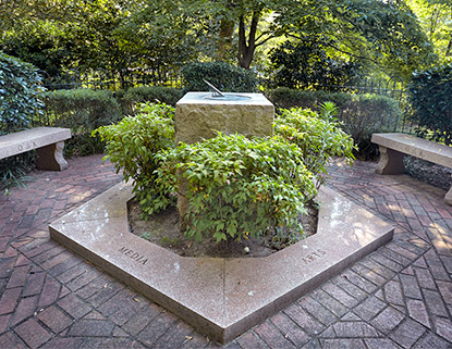 Stone sundial surrounded by bushes and brick pathways just off the historic Horseshoe. 