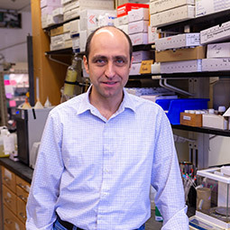 a man stands in a lab with a light blue button up shirt on smiling