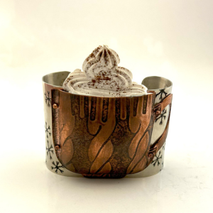 A wearable cuff bracelet by Christina McCurry. The mixed metal bracelet resembles a hot, cozy cup of coca topped with whipped cream and a sprinkle of cinnamon. 
