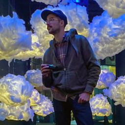 Alumnus Herman Phillips stands in an art installation filled with fluffy illuminated clouds.