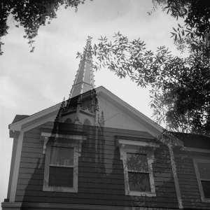 A black and white photograph by Veronica Matlosz. The composition is an overlay of my own home, overshadowed and haunted by a steeple, i.e. the house of God.