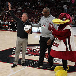 two people and Cocky on the USC basketball court