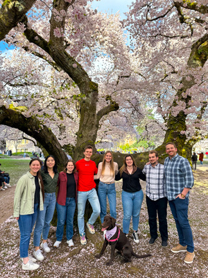 Nick Riley posing with his research group in front of a large flowering tree.