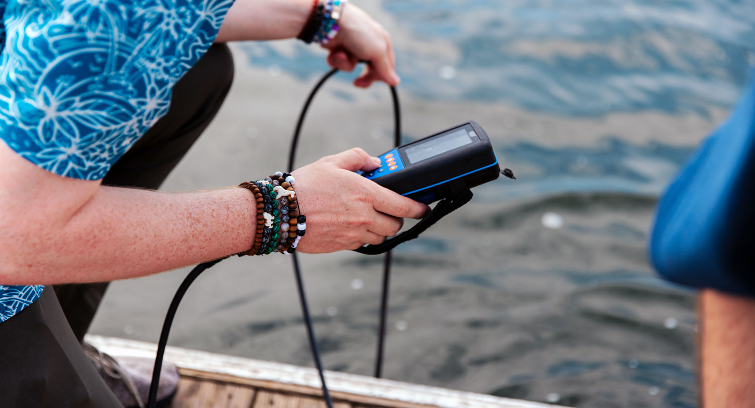 a person kneeling on a dock uses a meter to test water