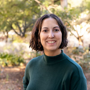 Woman stands outside with greenery in the background