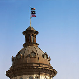 the american flag, south carolina flag and USC flag flying on top of the statehouse dome