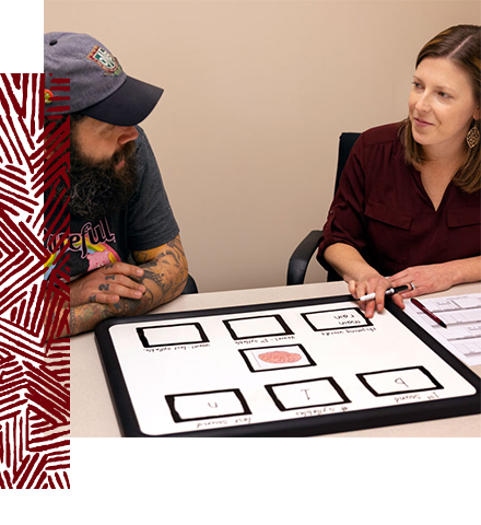 two people sit at a table with images on a large poster between them